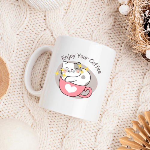 Cute white coffee mug with a smiling cat sitting in a pink heart cup and text Enjoy Your Coffee.